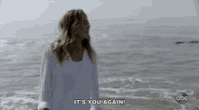 a woman standing on a beach with the words it 's you again above her