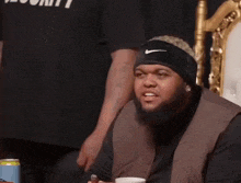 a man with a beard wearing a nike headband is sitting in a chair with a cup of coffee in his hand .