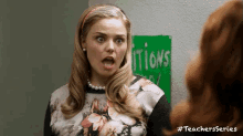 a woman is making a funny face in front of a green sign that says ' itions ' .