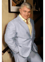 a man in a light blue suit and yellow shirt is leaning against a wall