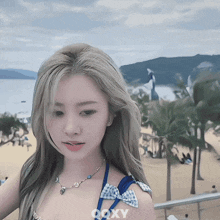 a woman wearing a bikini and a necklace with the word ooxy on the bottom right