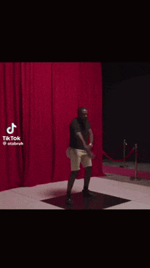 a man in a black shirt and white shorts is dancing in front of a red curtain