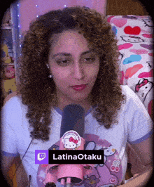 a woman with curly hair is sitting in front of a pink hello kitty microphone with the name latinaotaku on it