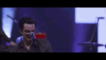 a man singing into a microphone with a drummer in the background