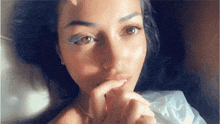 a close up of a woman laying on a bed with her hand on her mouth