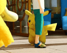 a person standing next to a pikachu that is looking at the camera