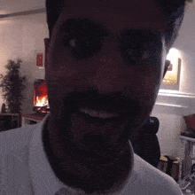 a man with a beard is smiling in front of a fireplace with a sign on the wall that says " no smoking "
