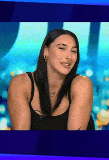 a woman in a black tank top is smiling with her eyes closed and her mouth open .
