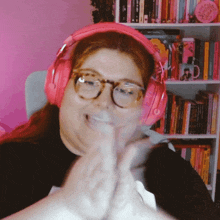 a woman wearing pink headphones and glasses stands in front of a bookshelf