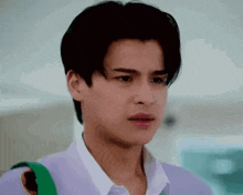 a young man is making a funny face while wearing a purple sweater and a white shirt .