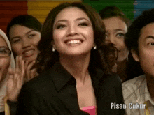 a woman is smiling in front of a group of people with pisau ukur written on the bottom right