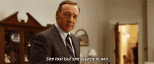 a man in a suit and tie is standing in a living room and saying `` she lost but she played to win . ''