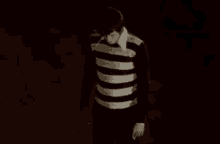 a man in a black and white striped sweater is walking in the dark .