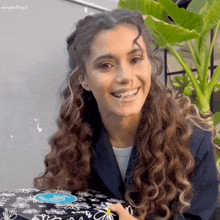 a woman with curly hair is smiling while holding a black box with flowers on it