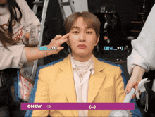 a man in a yellow jacket is getting his face painted by a woman with the word onew on the bottom