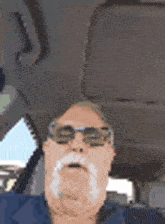 a man with a beard and sunglasses is sitting in a car .