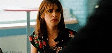 a woman in a floral shirt is sitting in front of a table