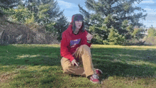 a person wearing a red hoodie is sitting in the grass smoking