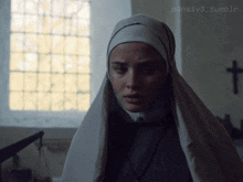 a nun with a veil on her head stands in front of a window with a cross on the wall
