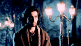 a man with long hair and a necklace is standing in front of street lights