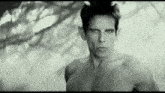 a black and white photo of a shirtless man standing in front of a tree .