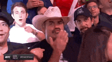 a man wearing a cowboy hat applauds while watching a ufc fight