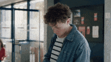 a young man with curly hair looks down in front of a sign that says ' a ' on it