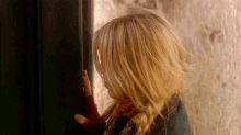 a little girl covering her face with her hand in front of a door
