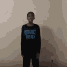 a young boy is standing in front of a wall wearing a black shirt with blue writing on it .