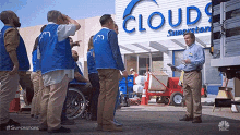 a group of workers are standing in front of a cloud 's superstore .