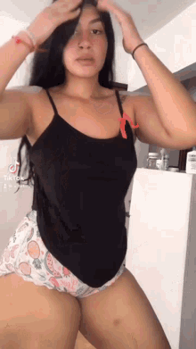 a woman in a black tank top and white shorts is standing in front of a refrigerator .
