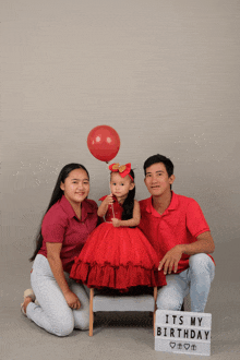 a little girl in a red dress is posing for a picture with her parents and a sign that says it 's my birthday