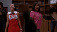 two cheerleaders wearing wmhs uniforms are singing in a room