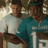 a man wearing a blue manatees jersey looks at a cell phone