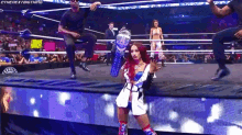a woman is holding a trophy in a wrestling ring while a man stands behind her .