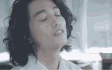 a man with long curly hair is sitting with his eyes closed and his mouth open .