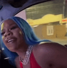 a woman with blue hair is sitting in the driver 's seat of a car and smiling .