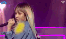 a woman is singing into a microphone on a stage with a purple background .