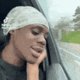 a man wearing a bandana is looking out of a car window .