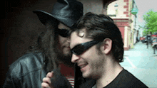 a man wearing sunglasses and a cowboy hat is talking into a microphone