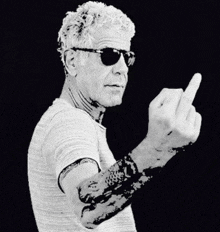 a man with a tattoo on his arm is giving the middle finger .