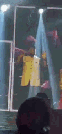 a man in a yellow jacket is standing on a stage in front of a crowd
