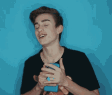 a young man in a black shirt is holding a blue iphone in his hands