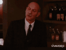 a man in a suit and tie is standing in front of a shelf with bottles on it and the word vivavideo at the bottom