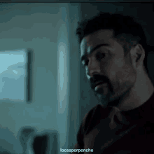 a man with a beard in a dark room with the words locasporponcho written below him