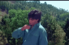 a man in a blue shirt is standing in front of a lush green forest .