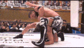 two men are wrestling in a ring with a crowd watching . one of the men is wearing knee pads .