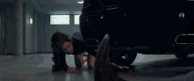 a woman is crawling on the floor next to a black car