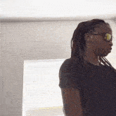a man with dreadlocks wearing sunglasses is standing in front of a window .