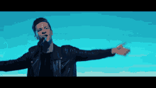 a man singing into a microphone with his arms outstretched in front of a blue sky
